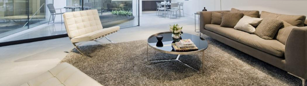 A glass table sits in the middle of a lounge with a single white chair and grey sofa either side.