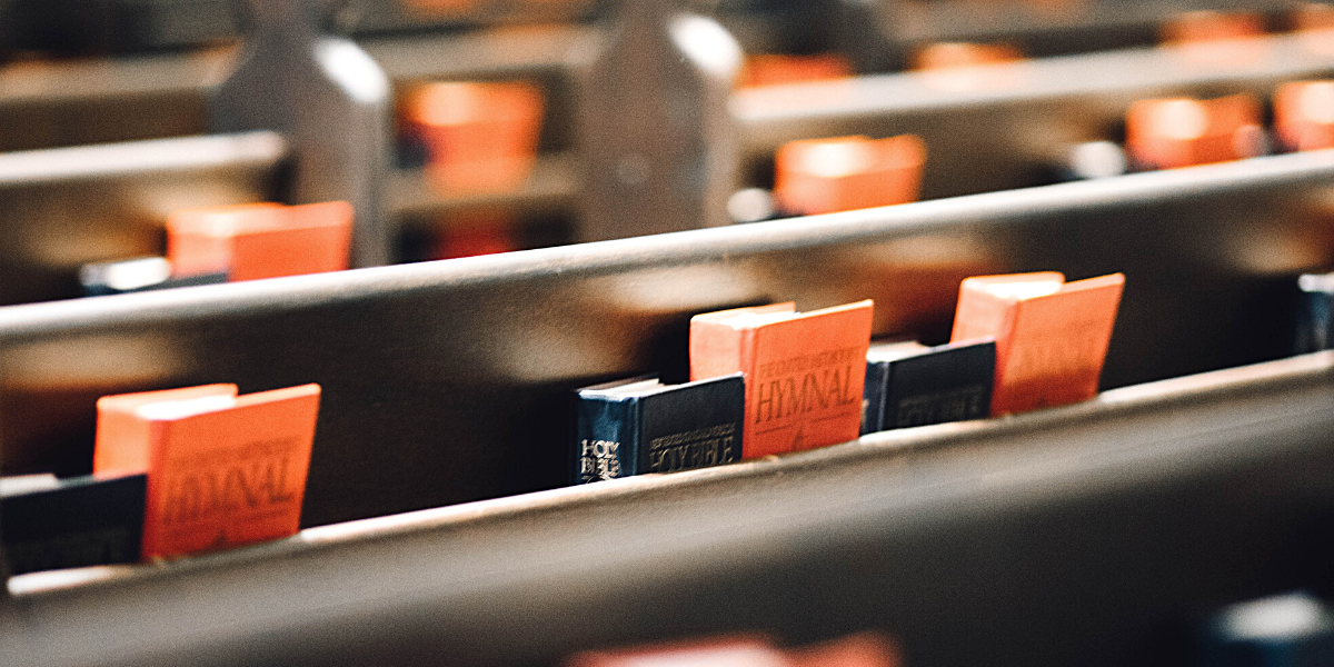 A photo graph of pews with a bible and hymn book in the pocket behind the pew