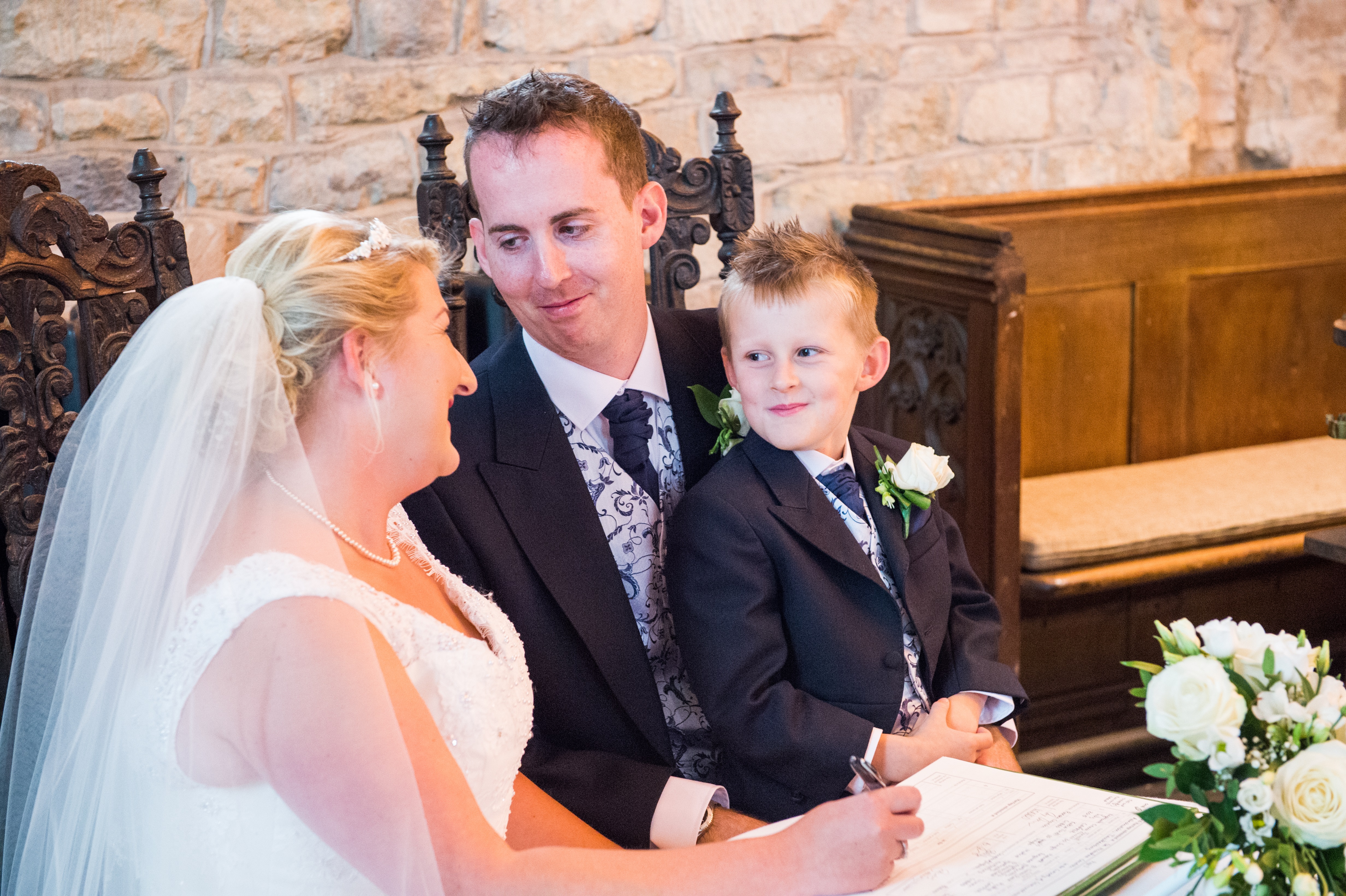 Bride and groom signing the register with their son on his dad's knee