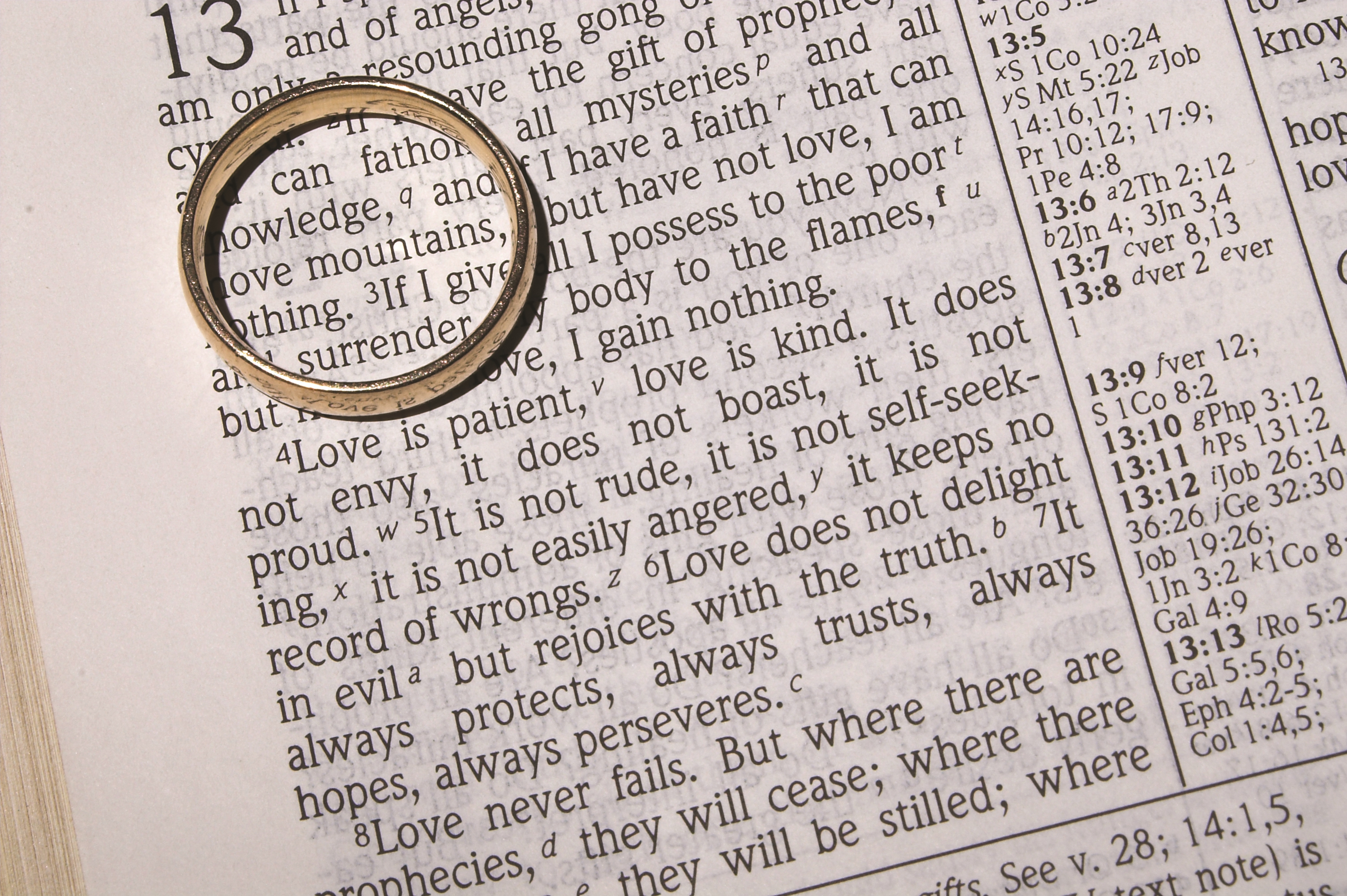 A close up of the Bible open at 1 Corinthians 13 with a wedding ring on the text
