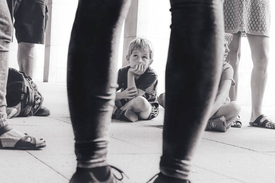 A boy sitting on the floor looking up at a group of adults in black and white.