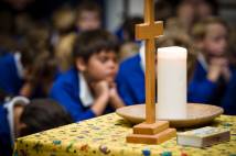 School children praying with cross and candle