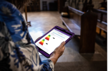 Someone standing in a church with an iPad showing emissions information for their church building.