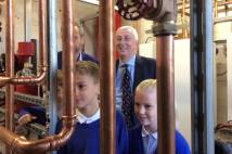 Older children from the school's "eco team" are joined by local MP, Speaker of the House of Commons, Sir Lindsay Hoyle MP. They are staring at new pipes that have been fitted as part of the project