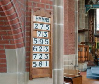 Close up of a hymn board on the wall in a church with several hymn numbers displayed
