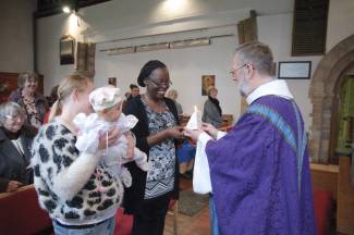 A vicar gives a candle to a godparent