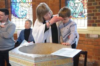 Vicar putting water on young boy's head near font