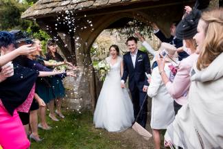 A newly married couple walk out from the lychgate during the confetti being thrown