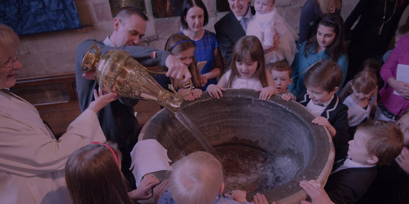 Children surrounding font, vicar pours in water