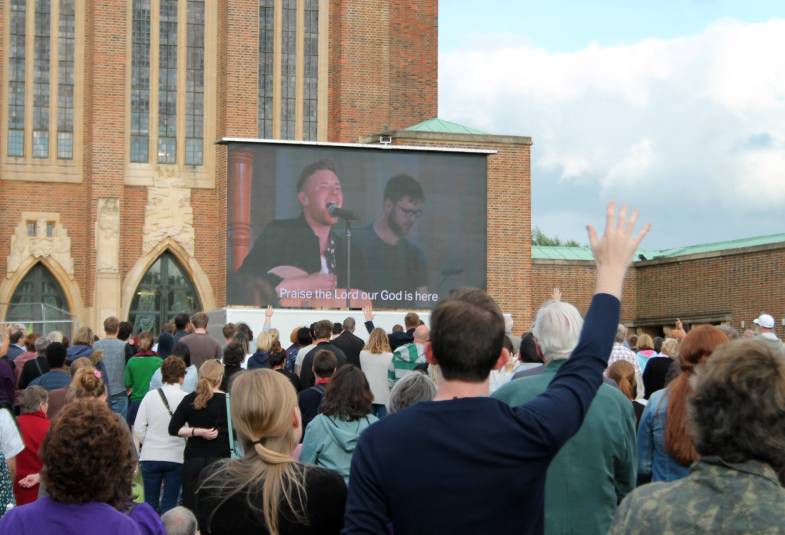 People taking part in service outside cathedral, watching singer on large screen