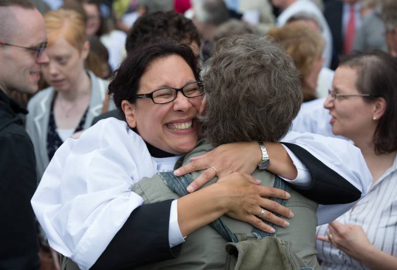 Female clergy member hugging friend and smiling 