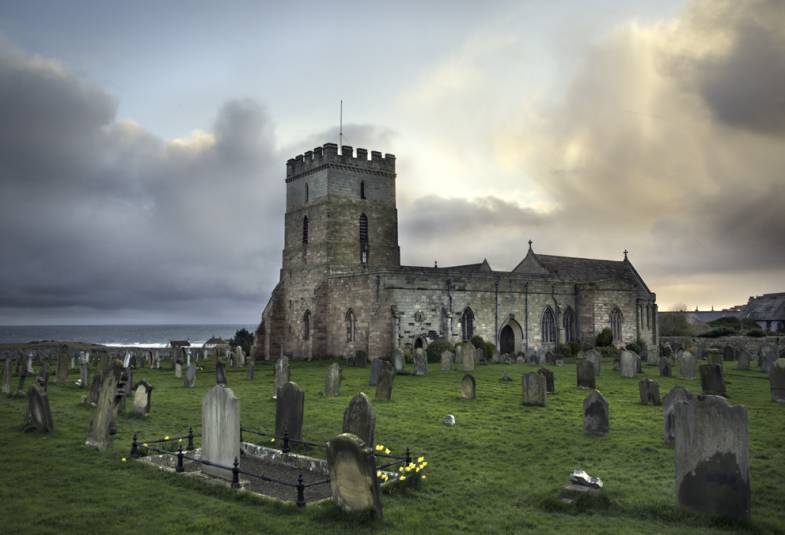 Church exterior with graveyard in foreground and sea in background