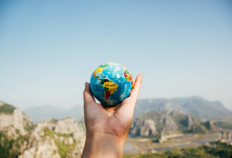 A hand holding a toy of planet Earth with rocky mountains in the background