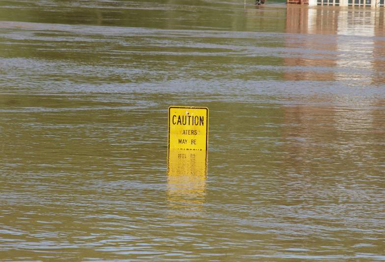 Water rising above a caution sign with a building in the background