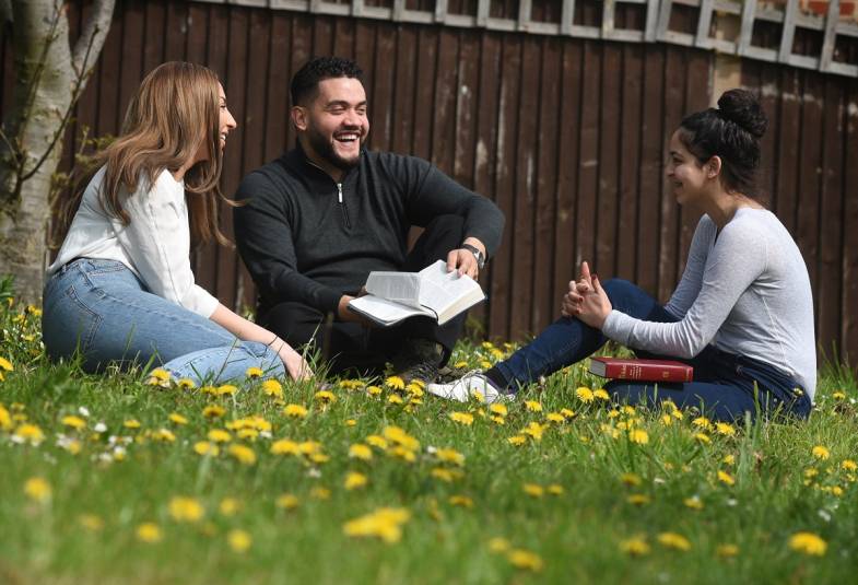Young adults sat on grass laughing with bible