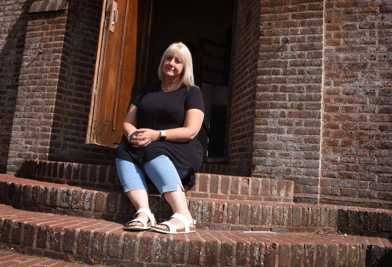 Lady in a black top and jeans wearing white sandals sitting outside an open church door