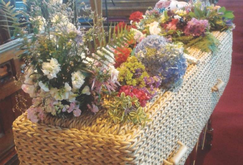 A wicker coffin in church with flowers laid on top