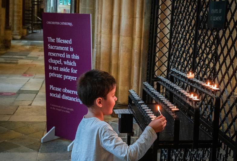 A child lights a votive candle in Chichester Cathedral