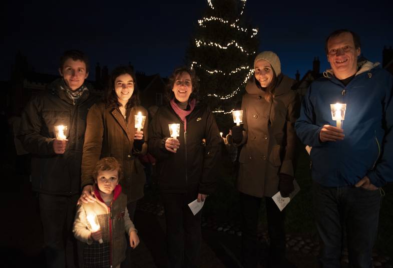 A family gather around a Christmas tree while holding candles