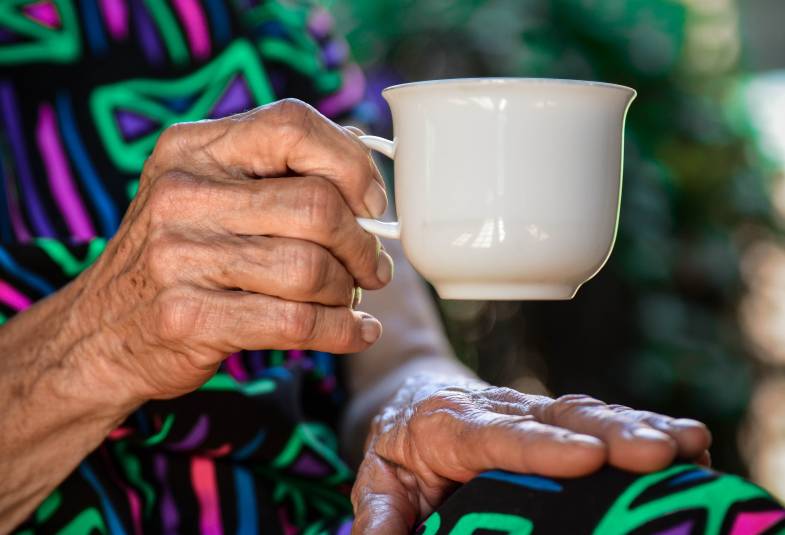 An older person with wrinkled hands drinks tea 