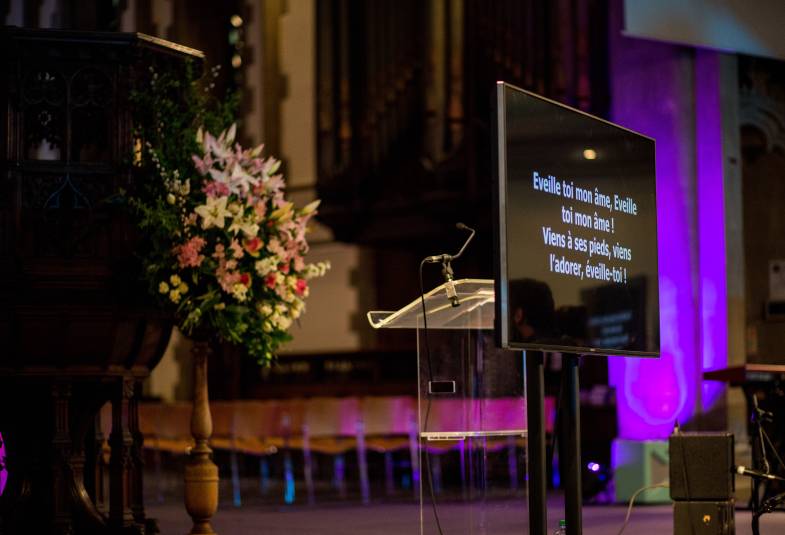 Lyrics to a hymn are shown on a projector screen next to a modern pulpit. A photo from French Connect and a photo from The Grove Community's Winter Wonderland, which it ran in 2019.