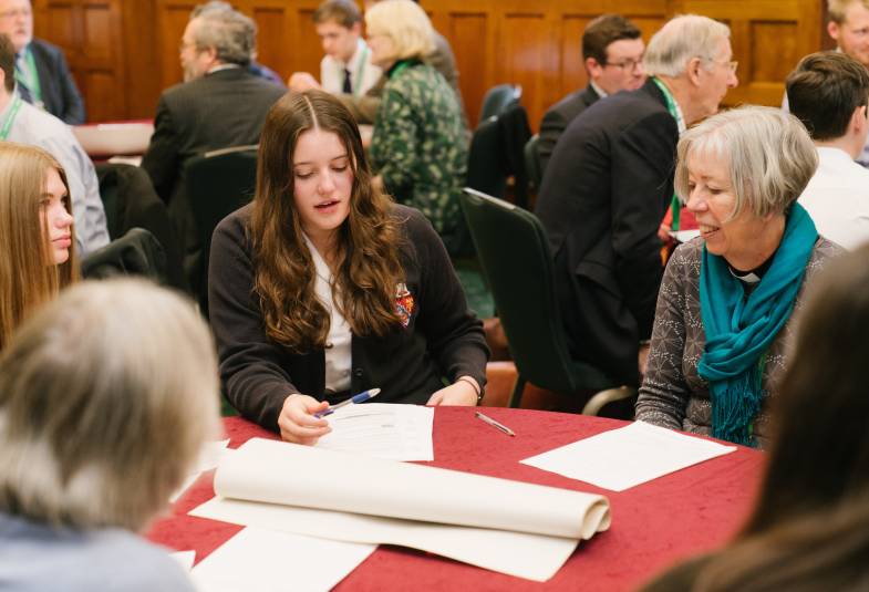 Children are shown engaging with older people around a table with notes in front of them as part of the Vision and Strategy break out rooms at General Synod