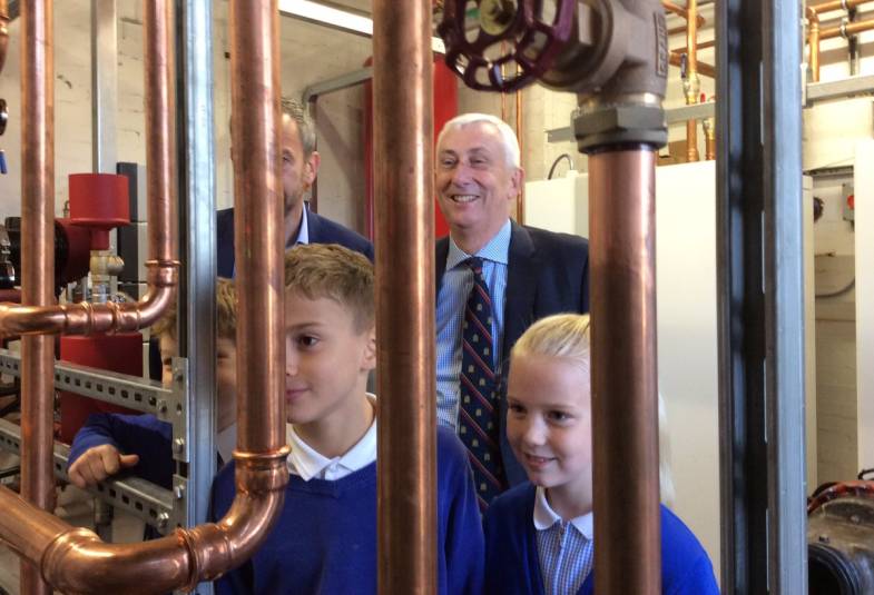 Older children from the school's "eco team" are joined by local MP, Speaker of the House of Commons, Sir Lindsay Hoyle MP. They are staring at new pipes that have been fitted as part of the project