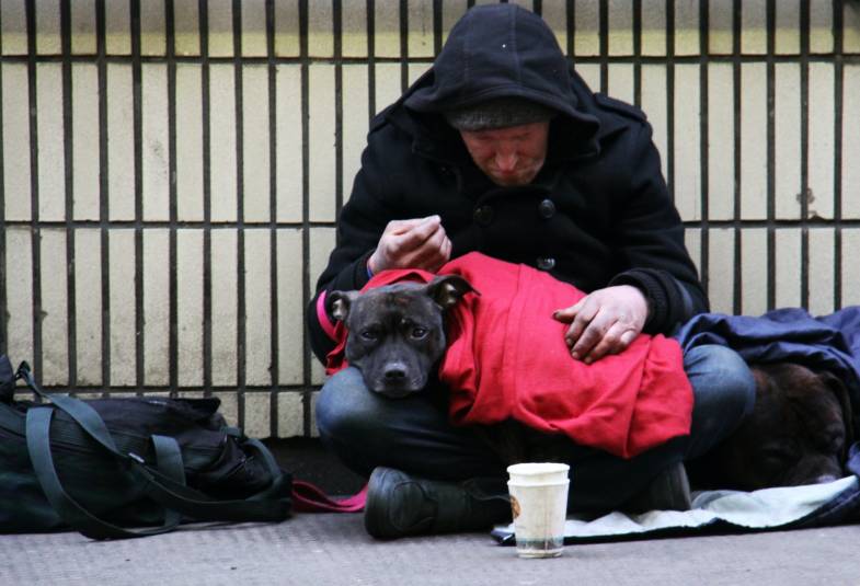 An homeless man is sat on the floor with a dog 