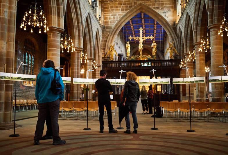 People are in the nave of Wakefield Cathedral with the lights lit up around them highlighting the size of the building