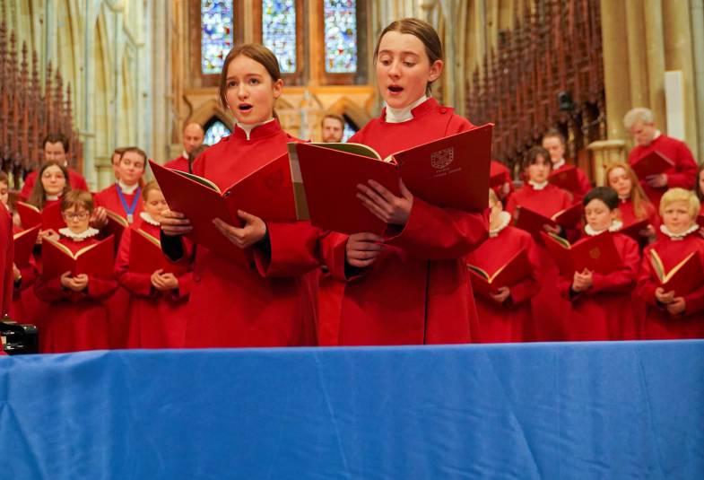 Female choristers are shown singing in red cassocks in the cathedral Truro nave and a Ukrainian flag in front of them