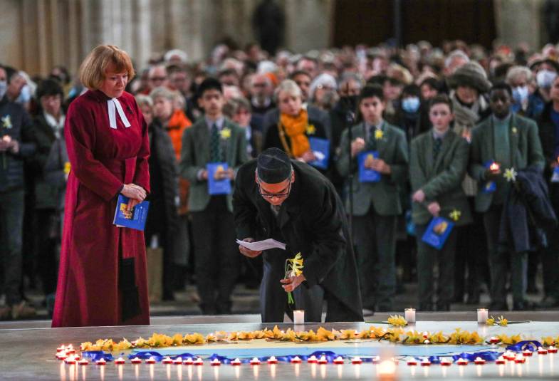 A man lays a flower at a memorial with a clergyperson standing beside them in a cathedral (Winchester)