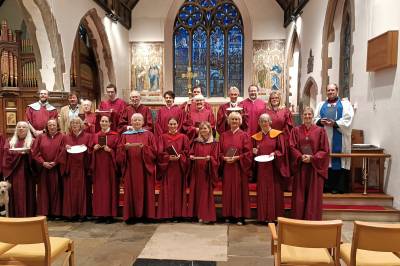 A choir in red robes stands smiling in the church of St Paul Without Walls in Canterbury 