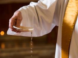 Clergy hand holding water filled shell for baptism 