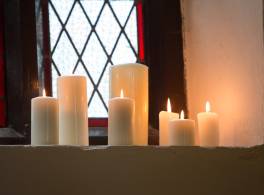 Group of lit candles in front of stained glass window