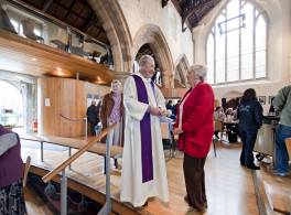vicar in robes, speaks to lady in church cafe