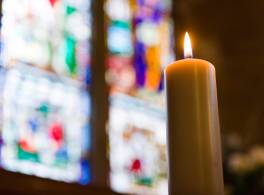 Lit candle in front of stained glass window