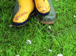 a child's bright yellow wellies standing on an adult's wellies in field with daisies