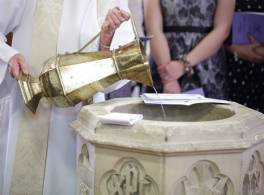 Close up of a large gold jug being used by a vicar to pour baptism water into a font