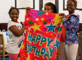 Three girls holding up a Happy Birthday banner
