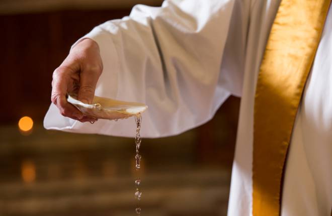 Clergy hand holding water filled shell for baptism 