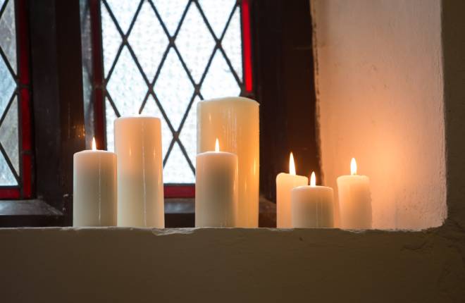 Group of lit candles in front of stained glass window