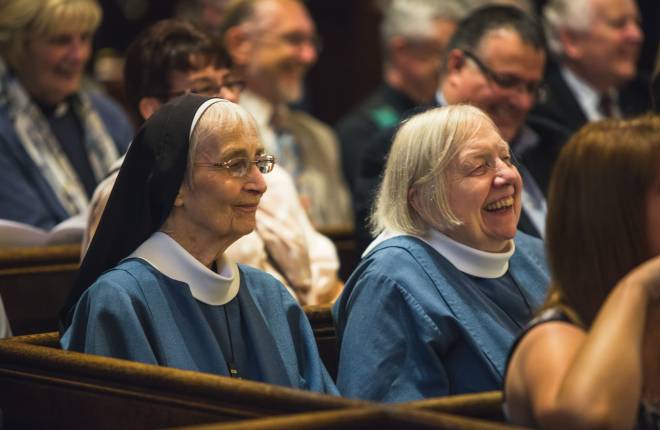 Two elderly nuns sitting in church pews together 