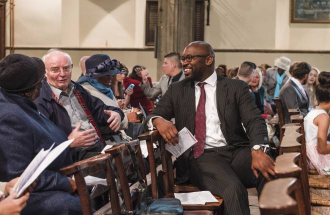 A man smiling on pew in church talking with other people