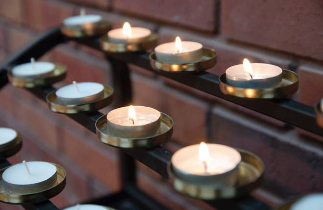 Rows of tea lights, some lit, some not, on a tea-light candle stand in a church