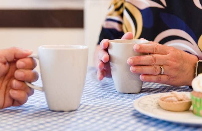 Close up of the hands of two people holding cups of tea