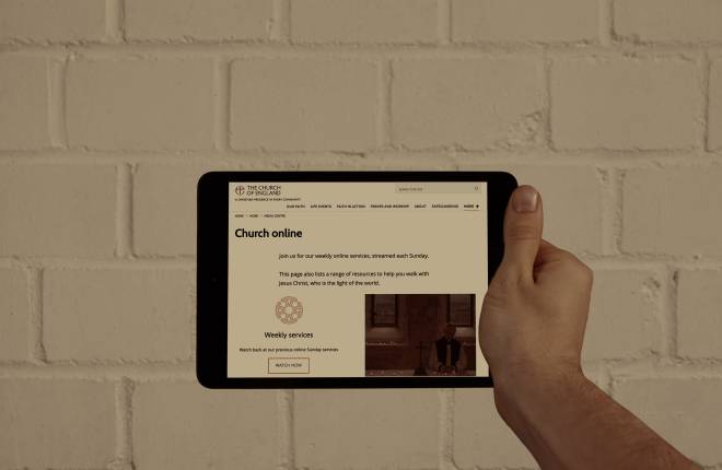 An iPad being held up against a brick wall with the Church of England website displayed.