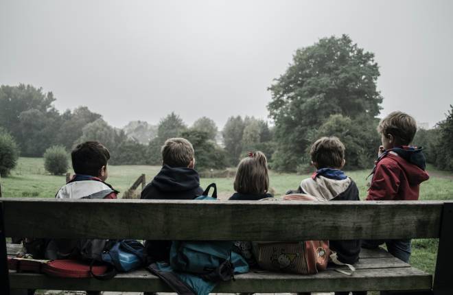 Five children sat on a bench looking out to a green park