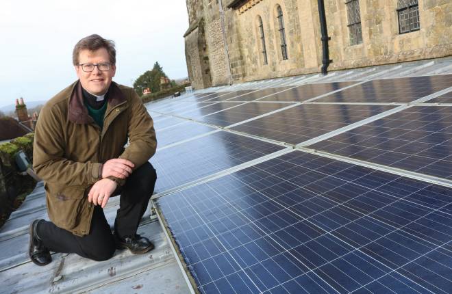 Vicar Will Hughes poses on the roof of a church with solar panels 