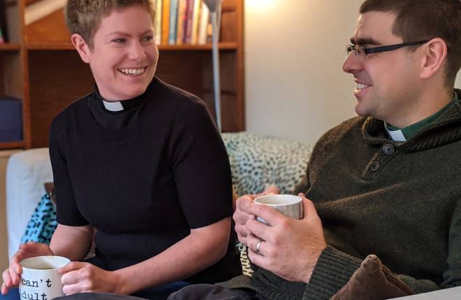 Two priests drink two while smiling at one another