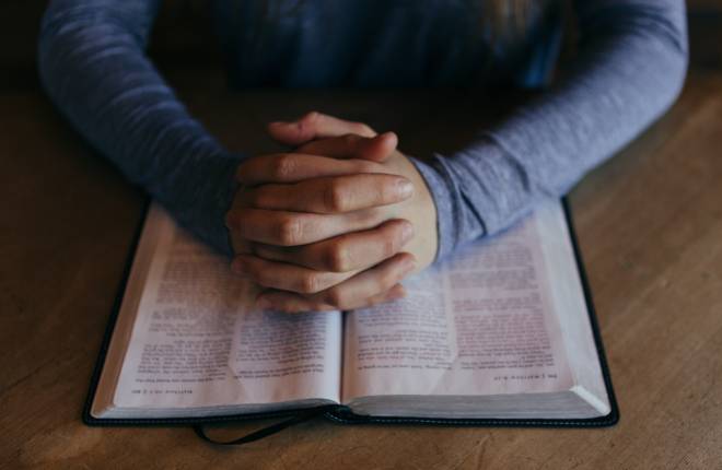 Hands clasped over a Bible in prayer.